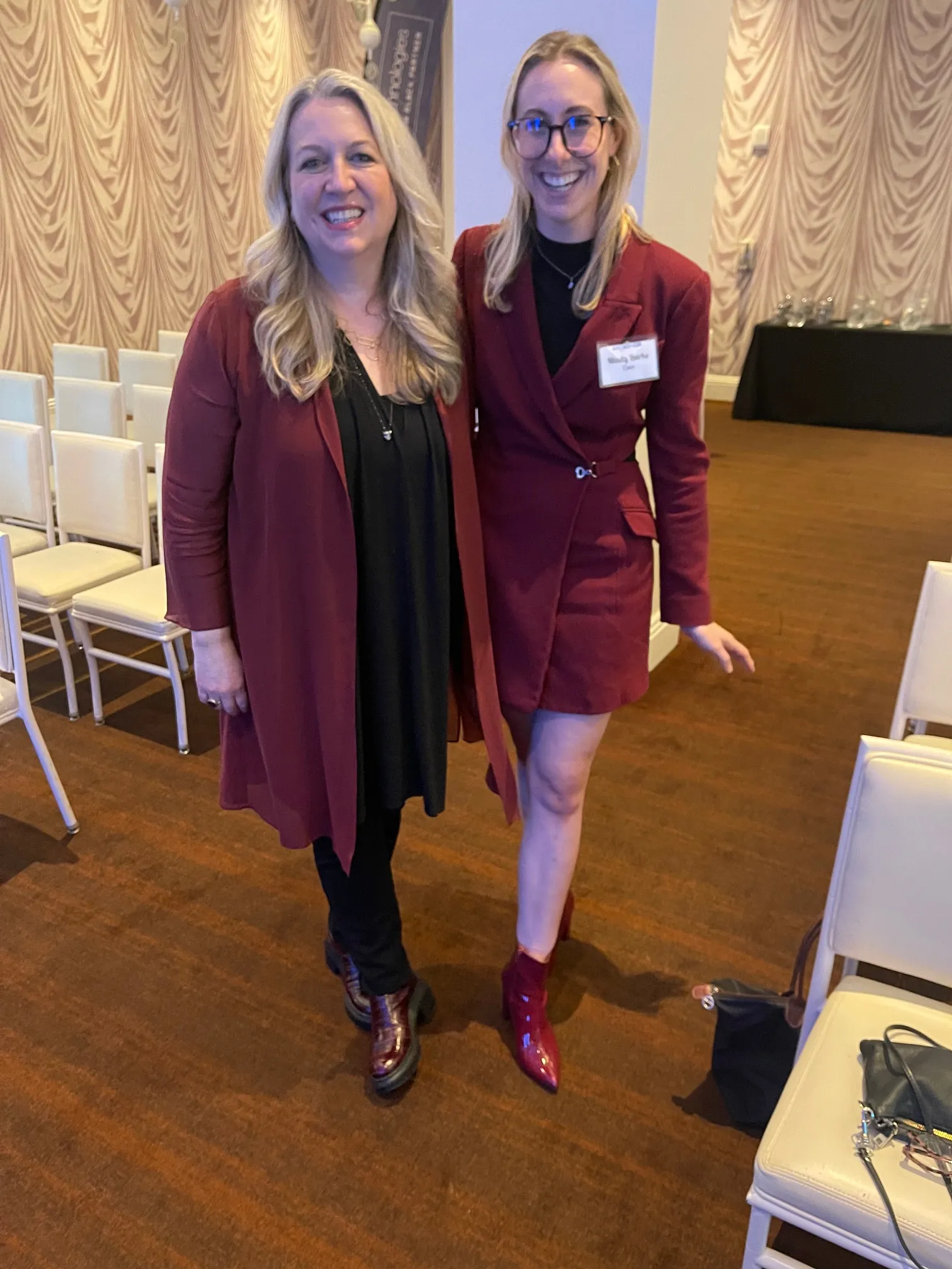Two smiling women in burgundy outfits standing together in an event room.