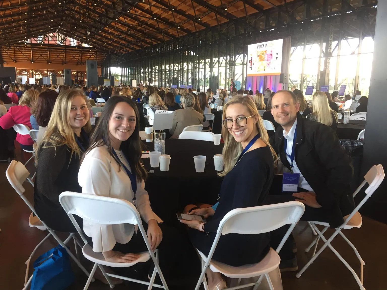 A group smiling around a table in a bright event hall.