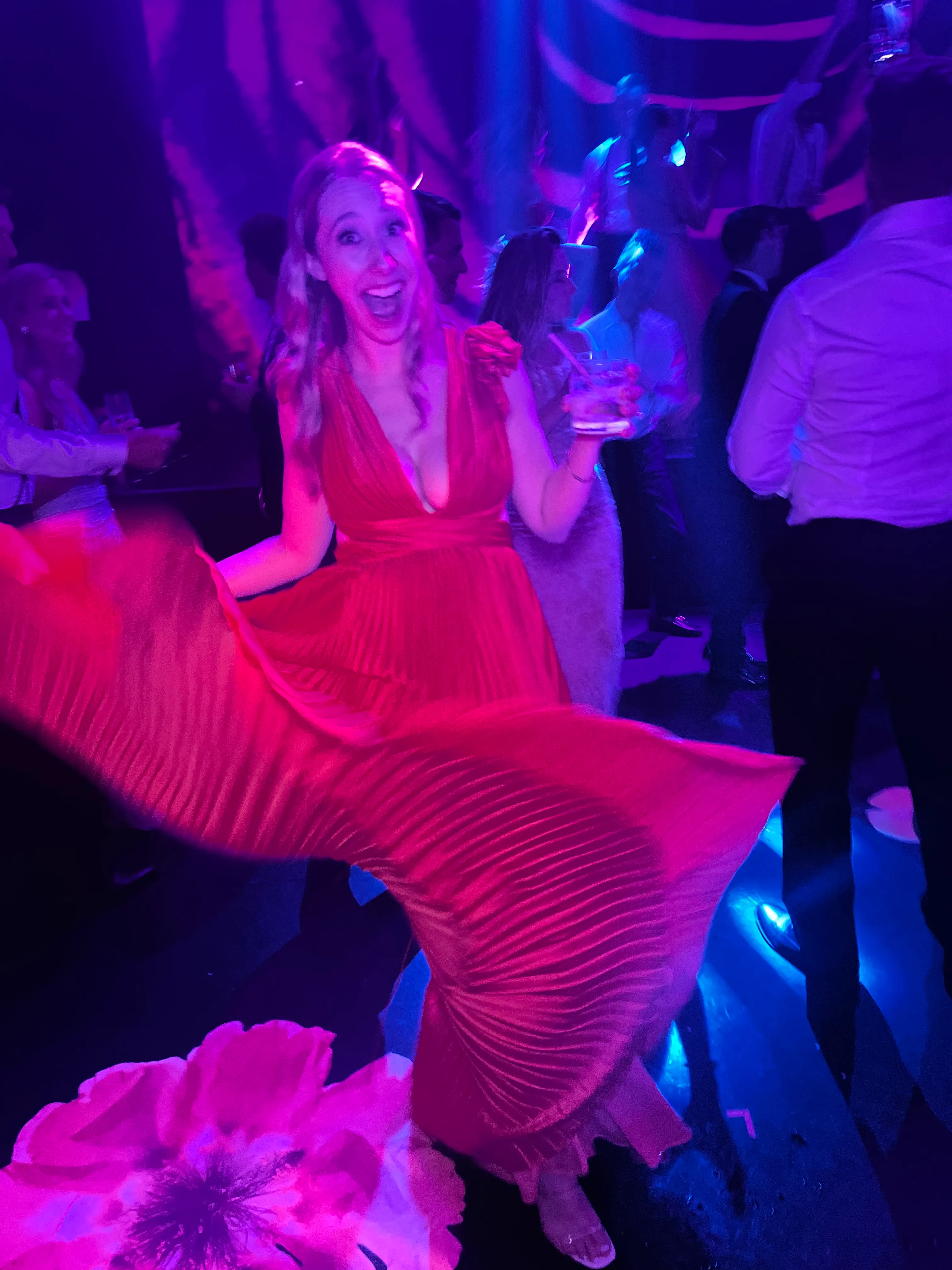 A woman twirling an orange gown under vivid purple and blue party lights.
