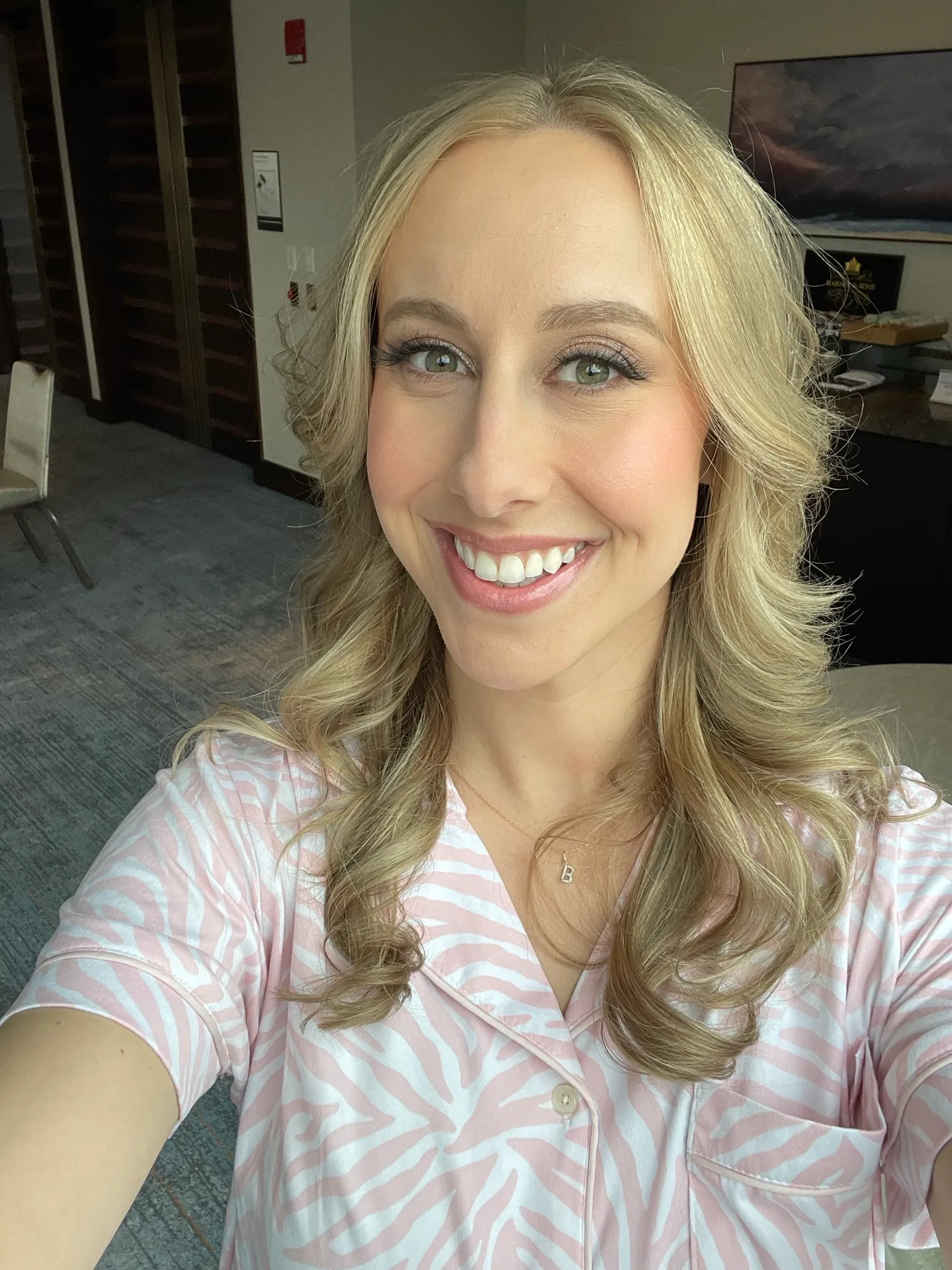 A smiling woman in a pale pink patterned top taking a portrait near a doorway.