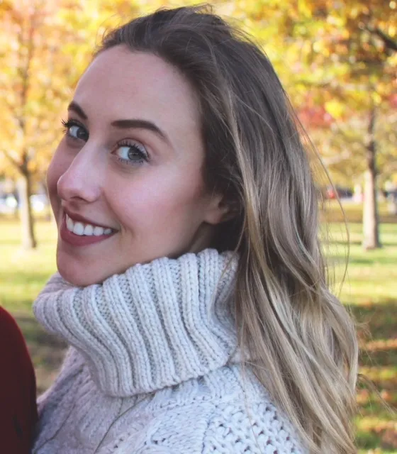 A woman in a knitted sweater looking over her shoulder among golden autumn leaves.