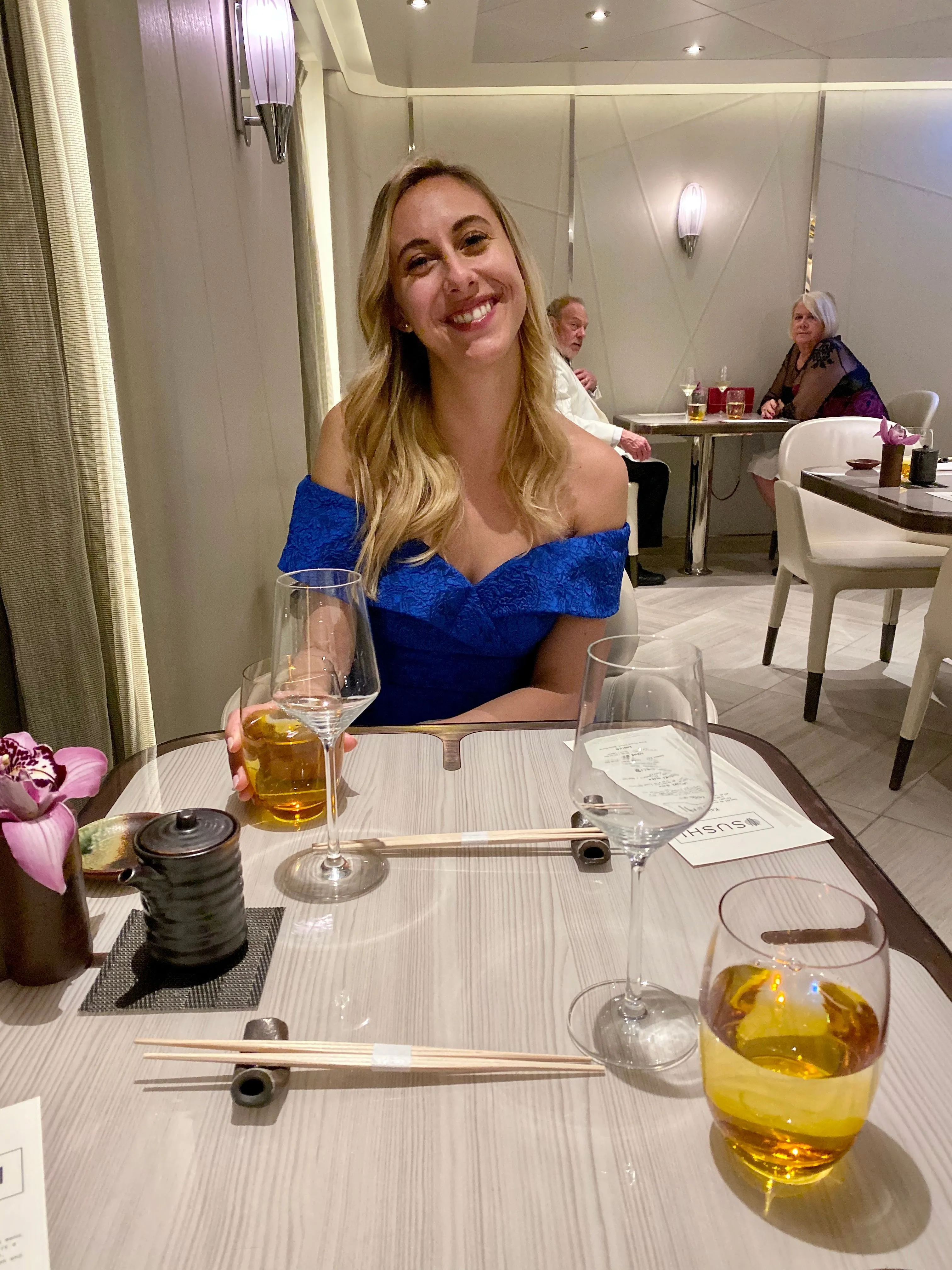 A woman in a blue dress smiling at a restaurant table.