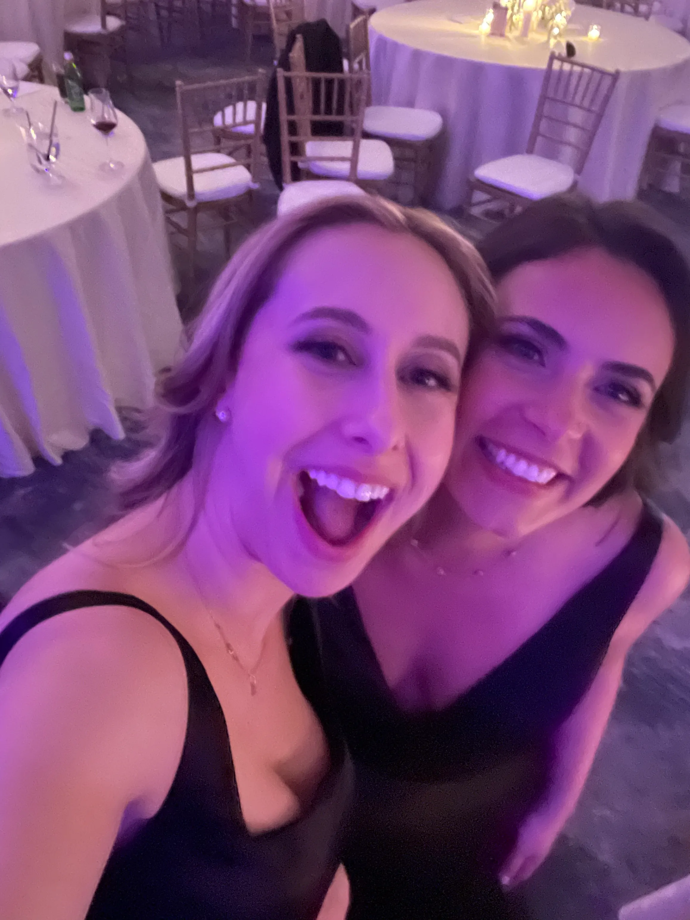 Two women smiling for a close-up photograph under violet party lighting.